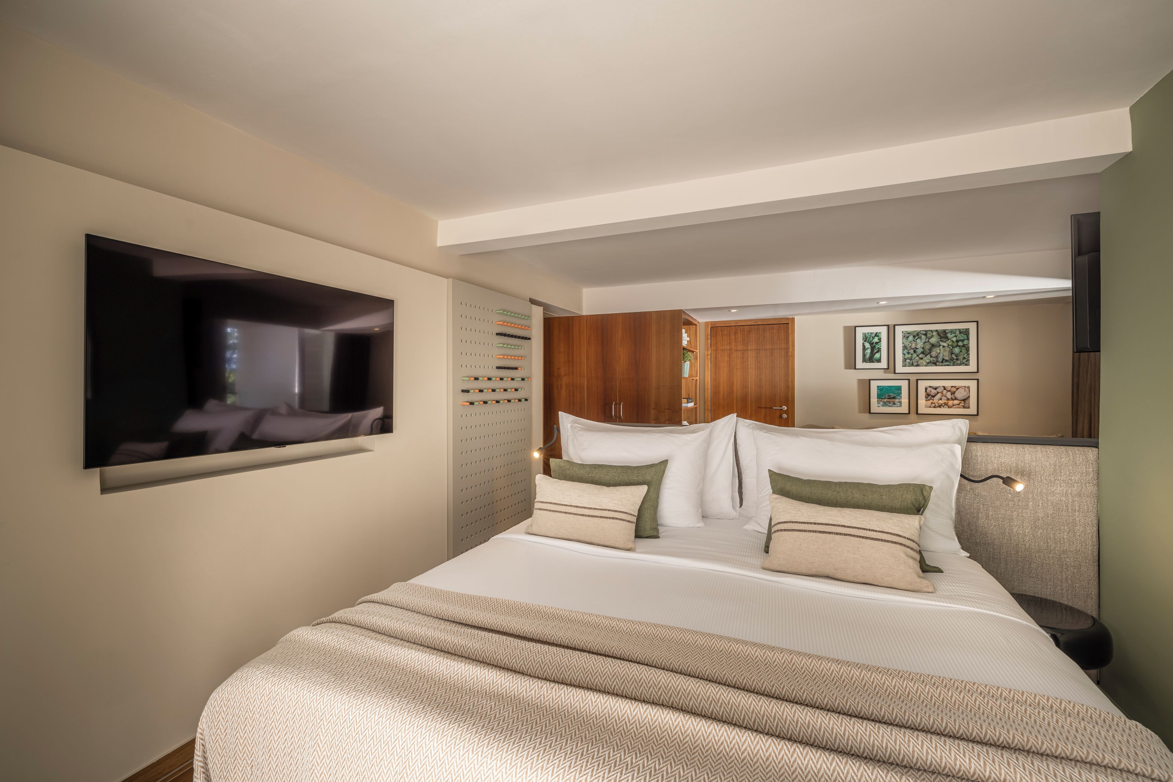 A hotel room with a bed, a television, a wardrobe, and a wall-mounted shelf with decorative items.