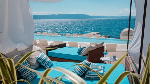 A balcony with a view of the sea, a pool, and a bed with blue bedding. - Girandella Resort, Valamar Collection (Labin)