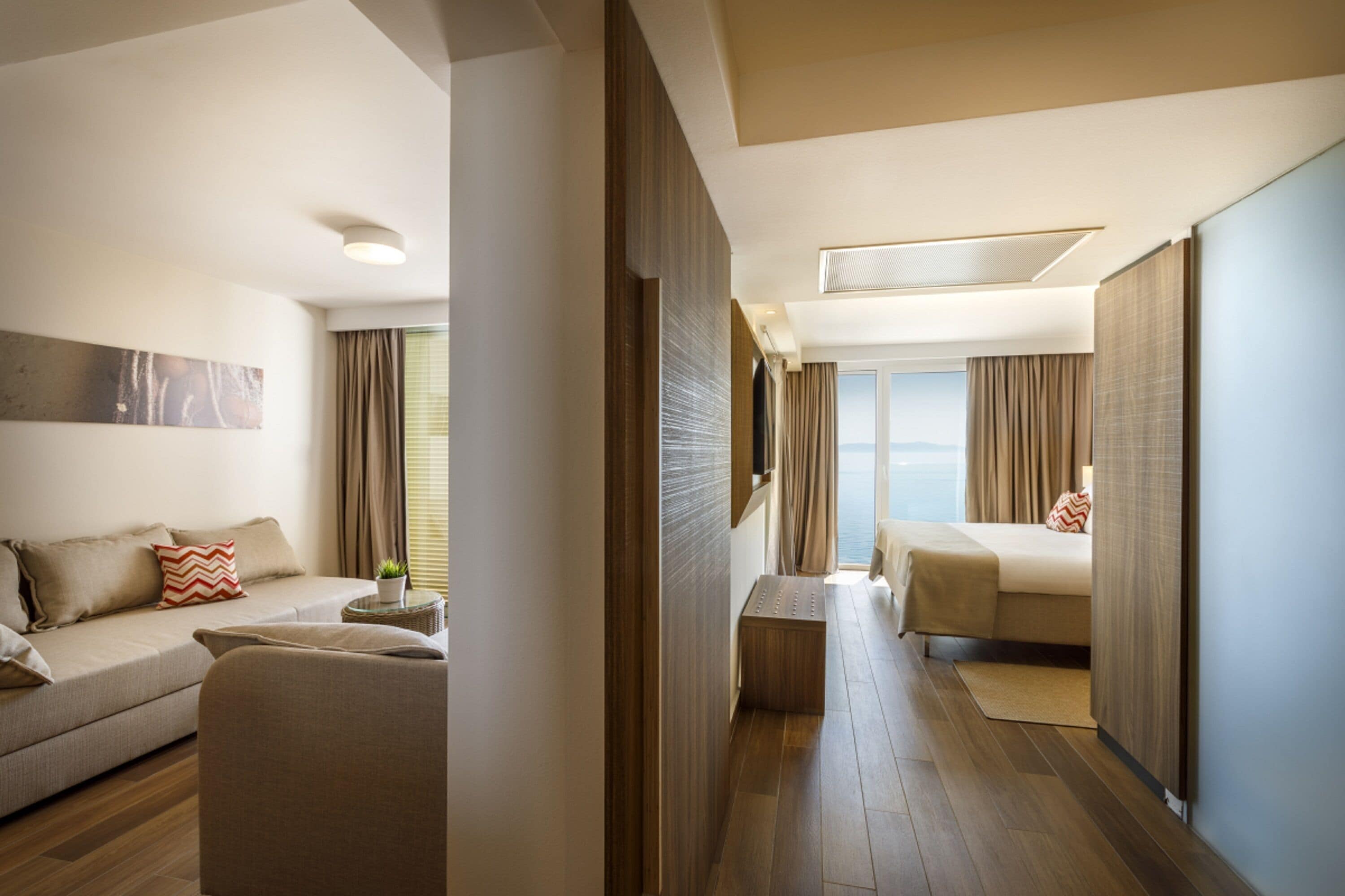 Ein modernes Hotelzimmer mit Sofa, Bett, einem kleinen Tisch mit Pflanze und Meerblick.