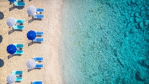 An aerial view of a beach with clear turquoise water and rows of blue lounge chairs and umbrellas. - Girandella Resort, Valamar Collection (Labin)