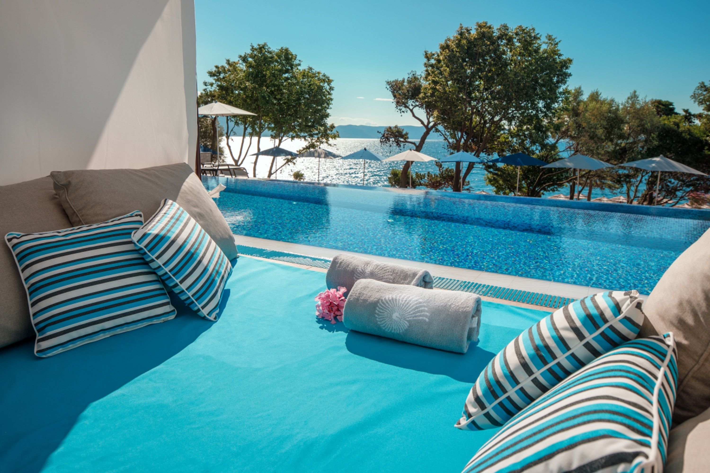 Un espace aménagé au bord de la piscine, avec vue sur la mer, comprenant des chaises longues et des parasols.