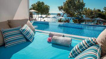 Un espace aménagé au bord de la piscine, avec vue sur la mer, comprenant des chaises longues et des parasols.