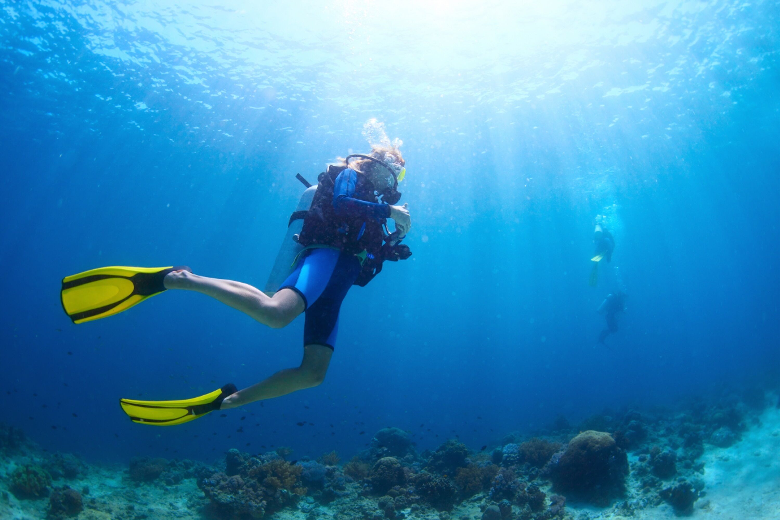 Un buceador bajo el agua con una cámara, rodeado de vida marina y formaciones de coral.
