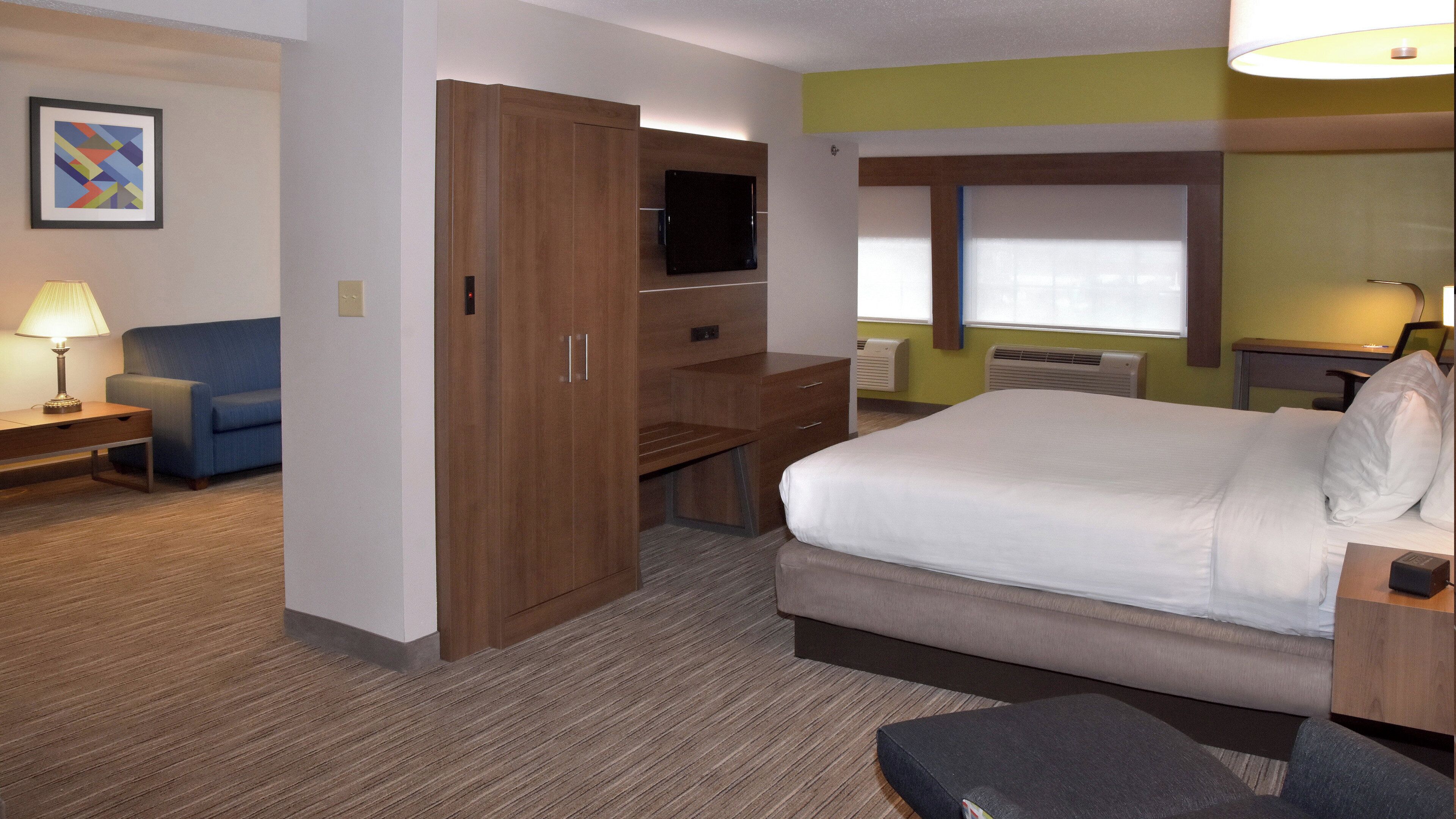 Een hotelkamer met een bed, bureau, televisie, stoel, lamp en een schilderij aan de muur.