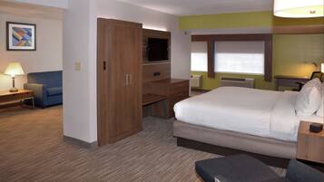 Een hotelkamer met een bed, bureau, televisie, stoel, lamp en een schilderij aan de muur.