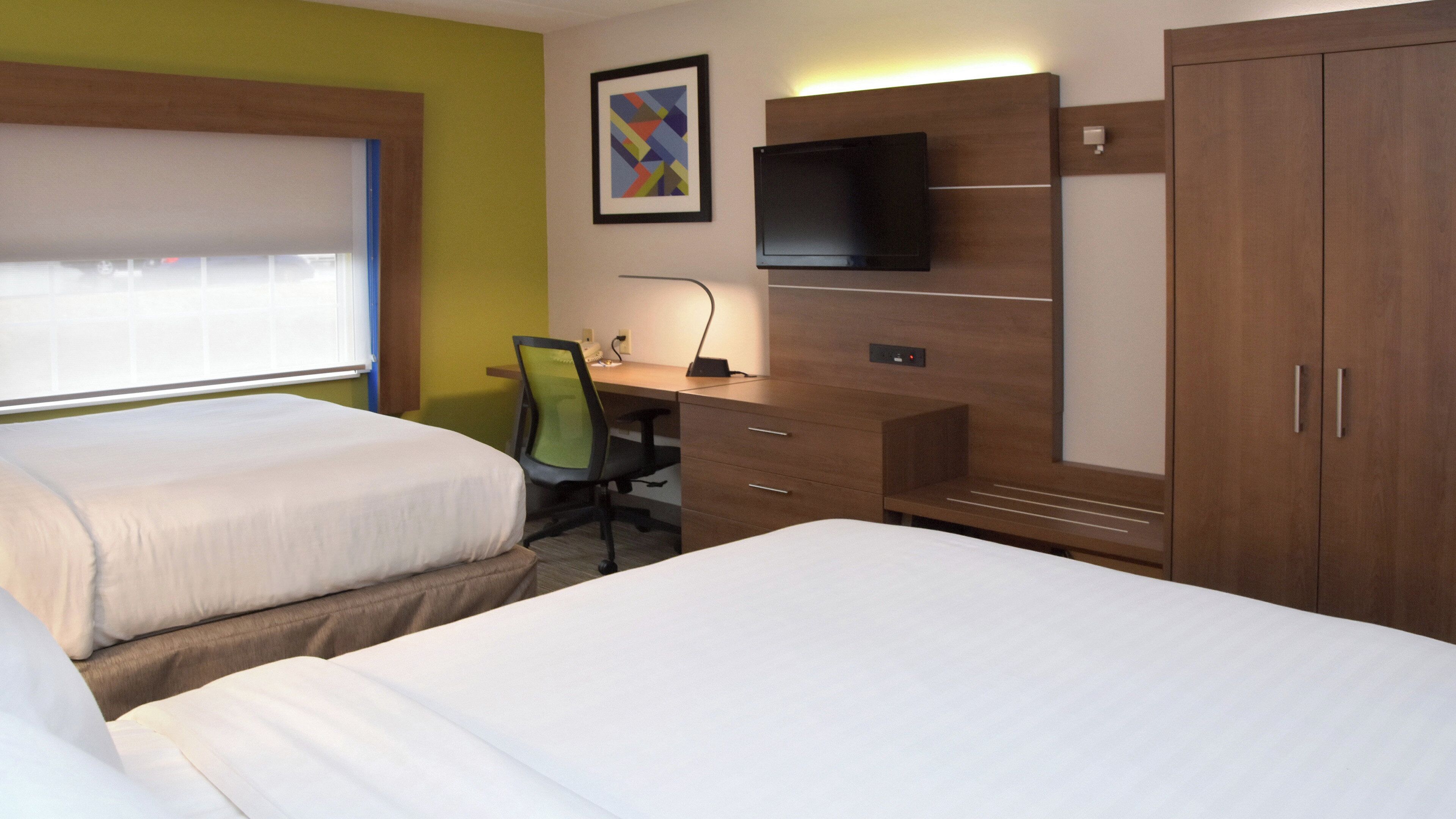 A hotel room with two beds, a desk, a chair, a TV, and a wardrobe.
