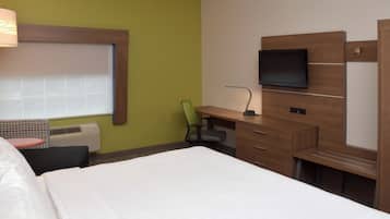 A hotel room with a bed, a desk with a chair, a television, and a window with blinds.