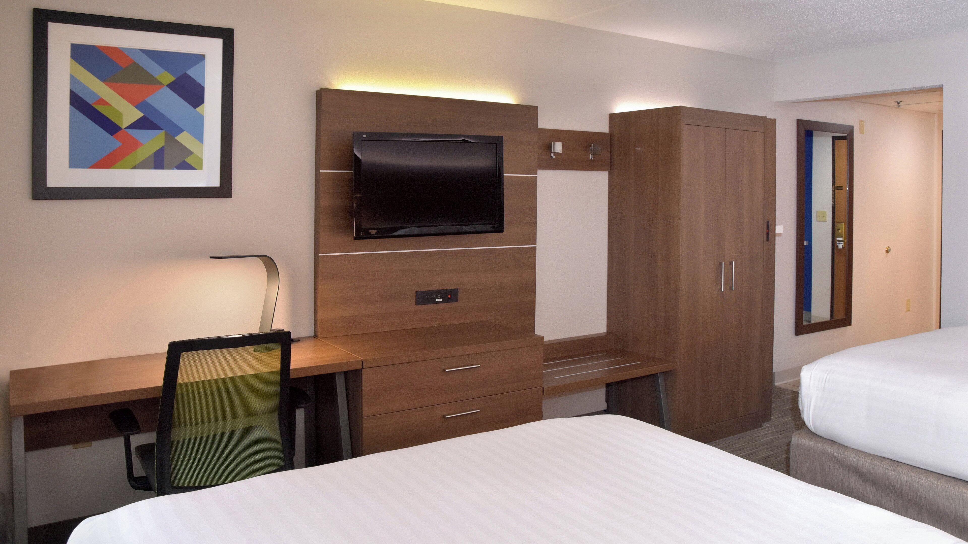A hotel room with a bed, a desk with a chair, a television, and a wardrobe.