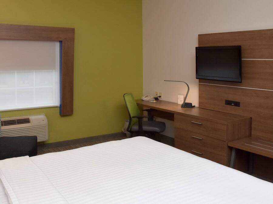 A hotel room with a bed, a desk with a chair, a television, and a window with blinds.