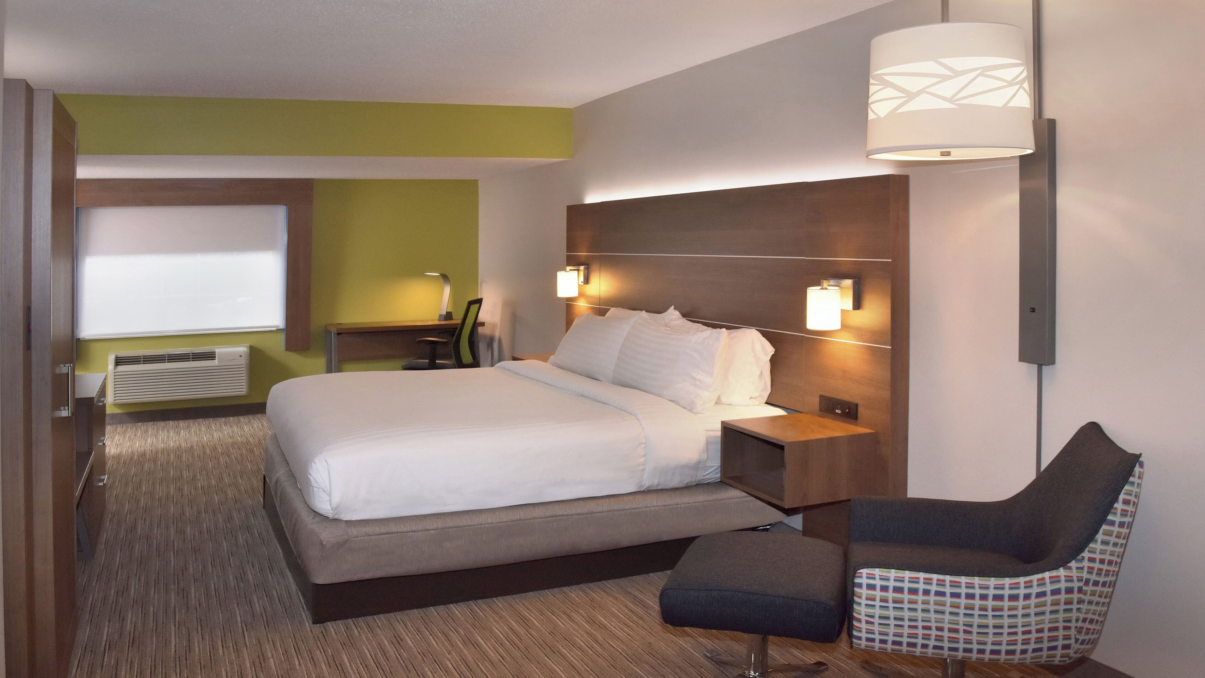 A hotel room with a bed, bedside tables, a desk, a chair, and a wall-mounted lamp.