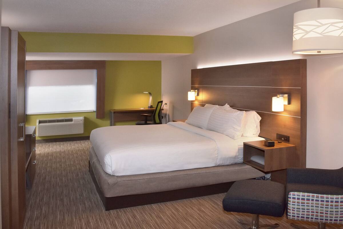 A hotel room with a bed, bedside tables, a desk, a chair, and a wall-mounted lamp.