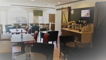 Un comedor con mesas y sillas, una estación de café y un reloj en la pared.