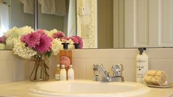 A bathroom sink with toiletries, a mirror, and a vase of flowers.