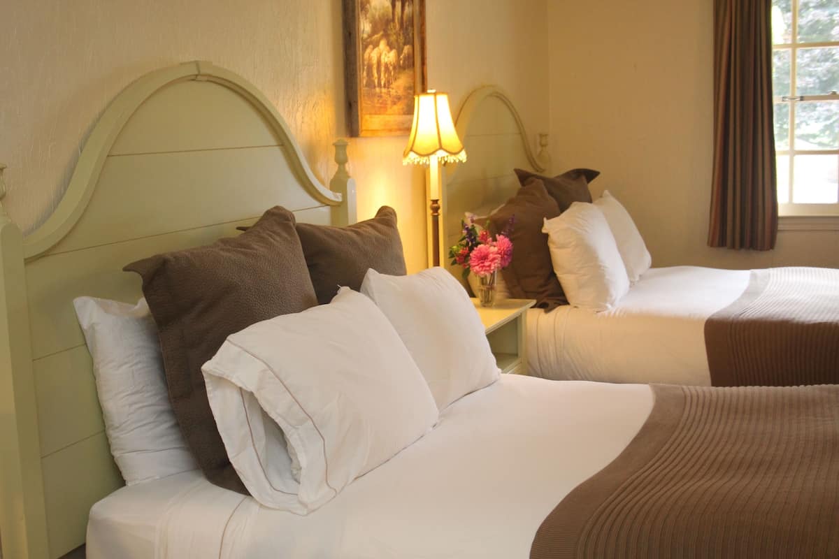 A hotel room with two beds, a lamp, and a painting on the wall.