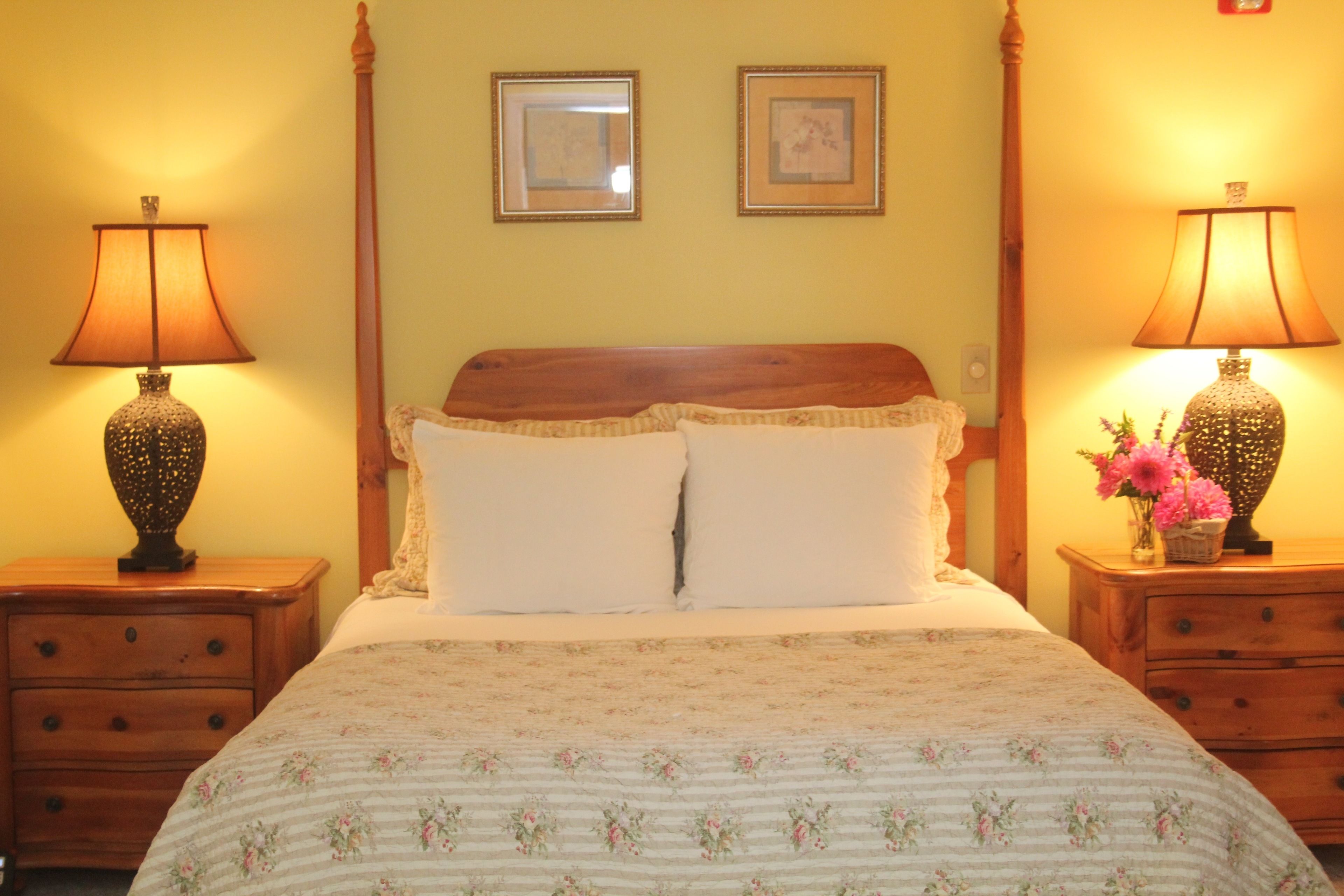 Una camera da letto con un letto di legno, due comodini con lampade e due quadri appesi al muro.
