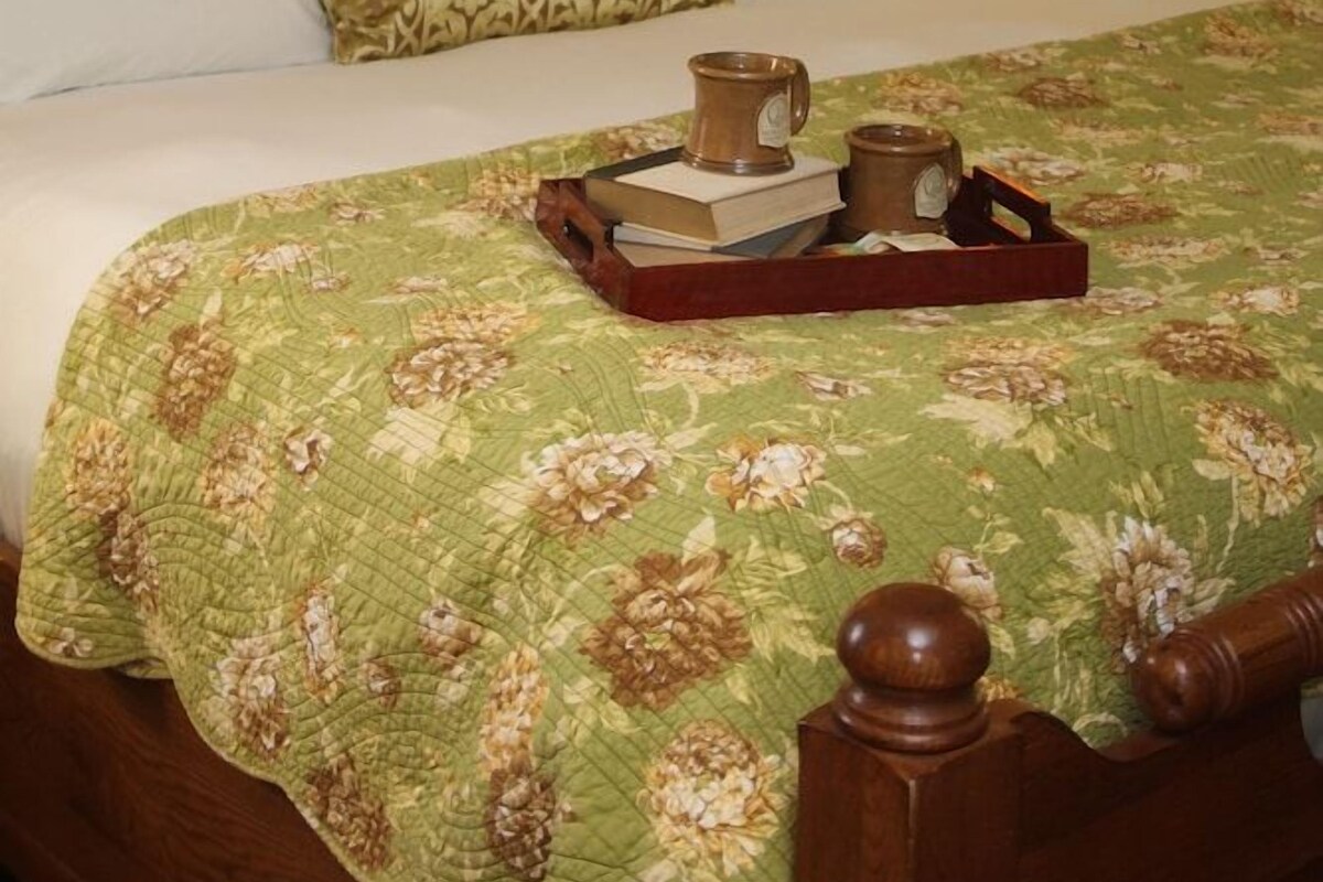 Una cama bien hecha con colcha floral, cabecero de madera y lámpara de noche.