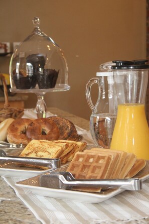 A breakfast tray with bagels, waffles, and a glass of orange juice.
