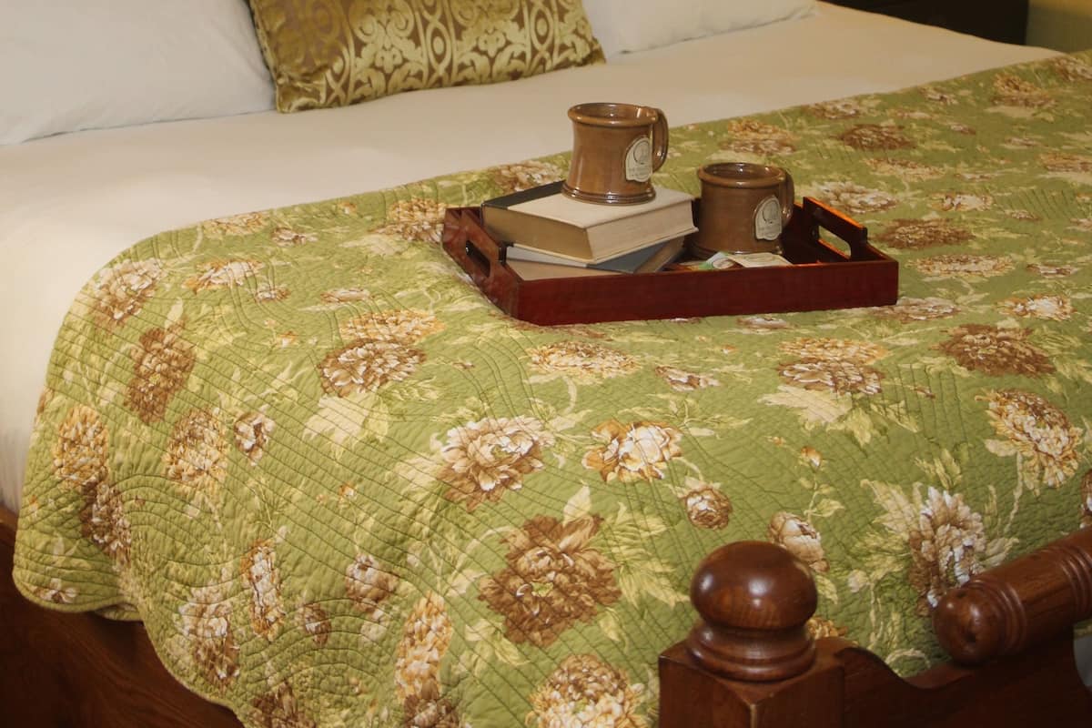 A neatly made bed with a floral bedspread, pillows, and a tray with books and mugs.