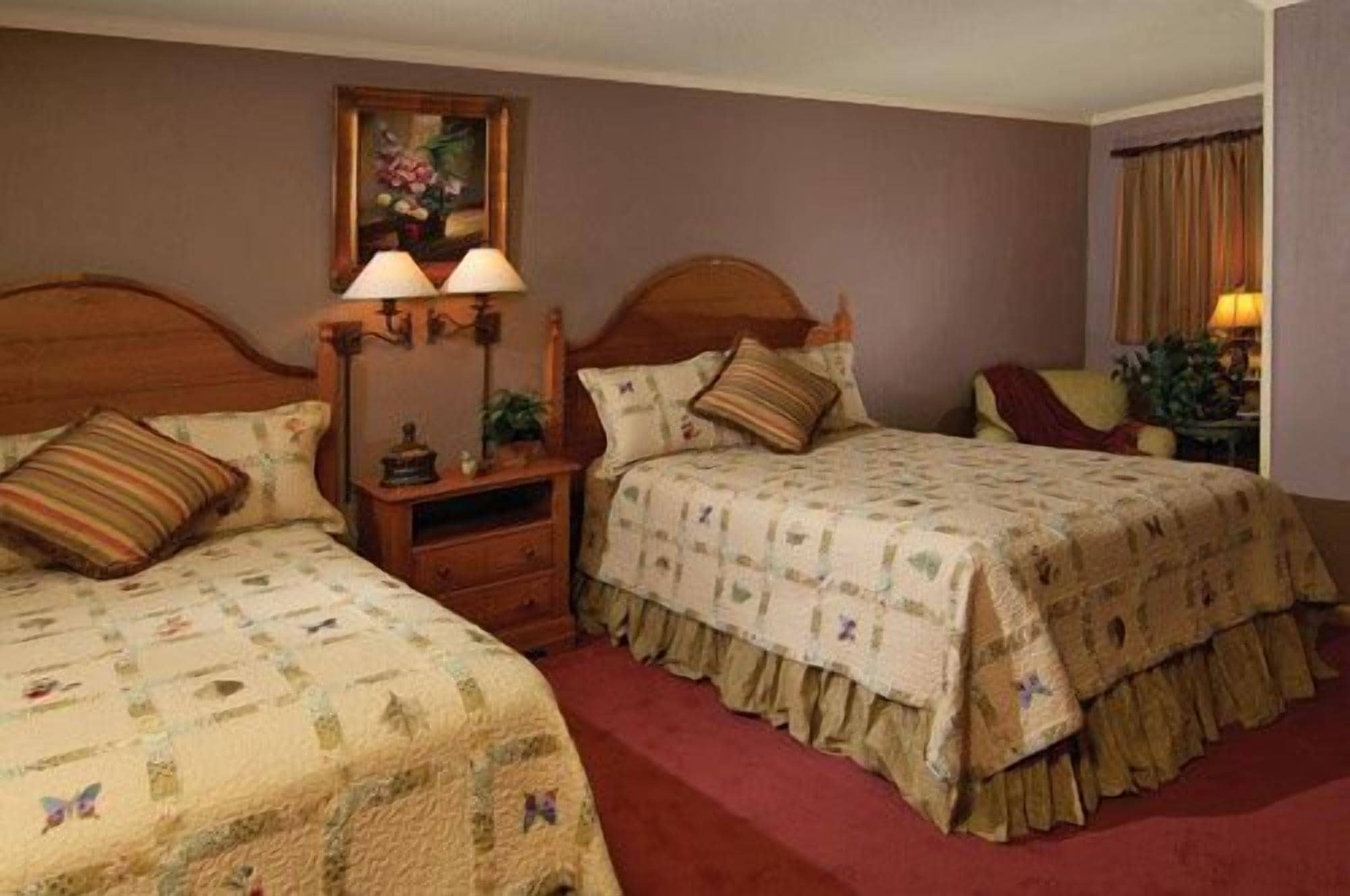 A bedroom with two beds, a nightstand with lamps, a dresser, and a painting on the wall.