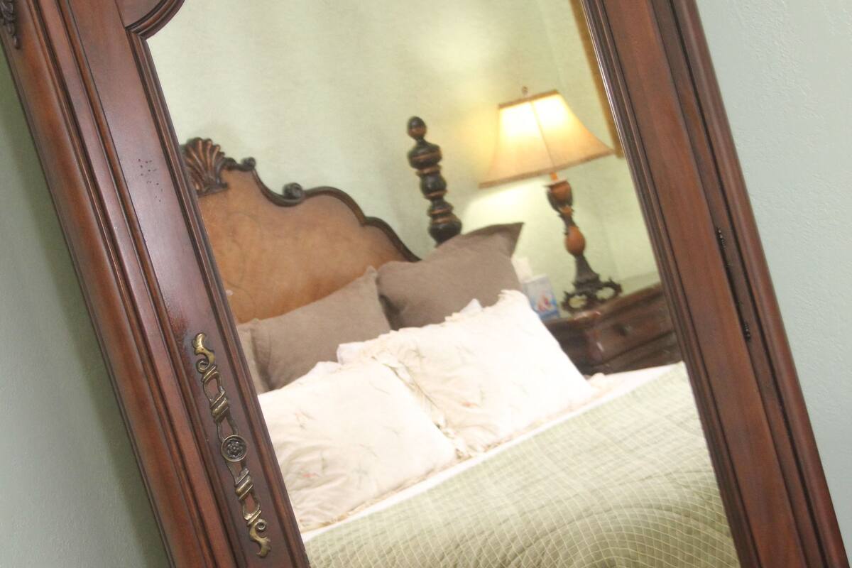 A mirror with a wooden frame reflecting a bed with a green bedspread and white pillows.