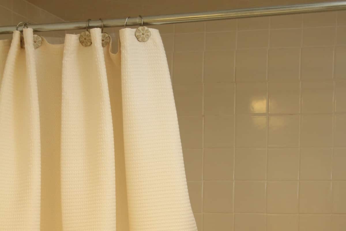 A bathroom with a beige tiled wall, a shower curtain, and a soap dispenser.