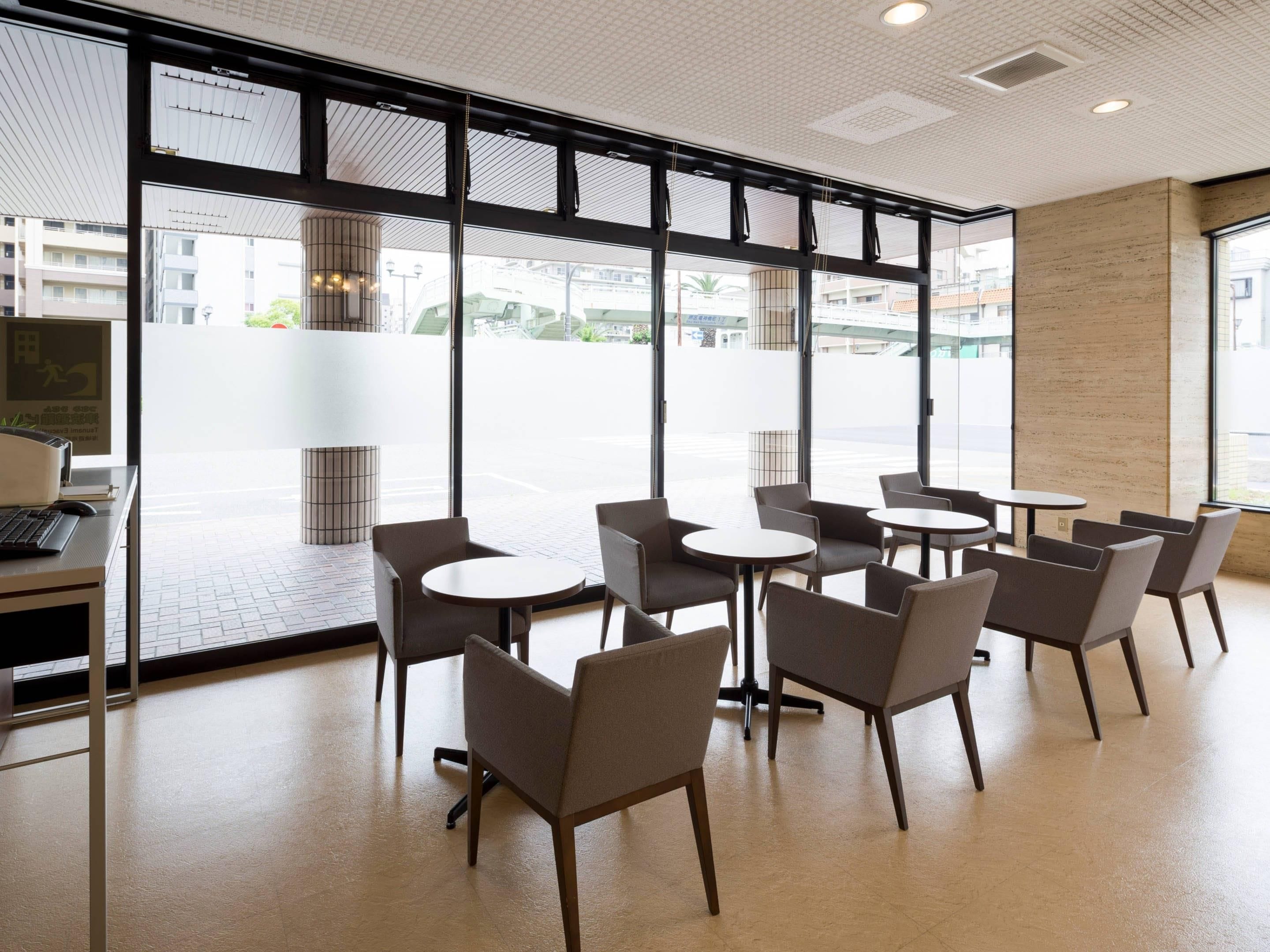 A modern cafe interior with round tables and chairs, large windows, and a view of the street.