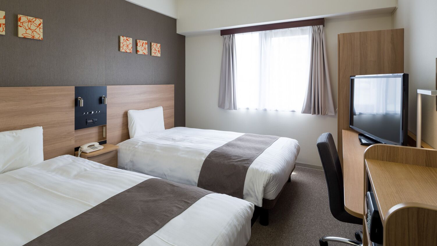 A hotel room with two beds, a desk, a TV, and a phone.
