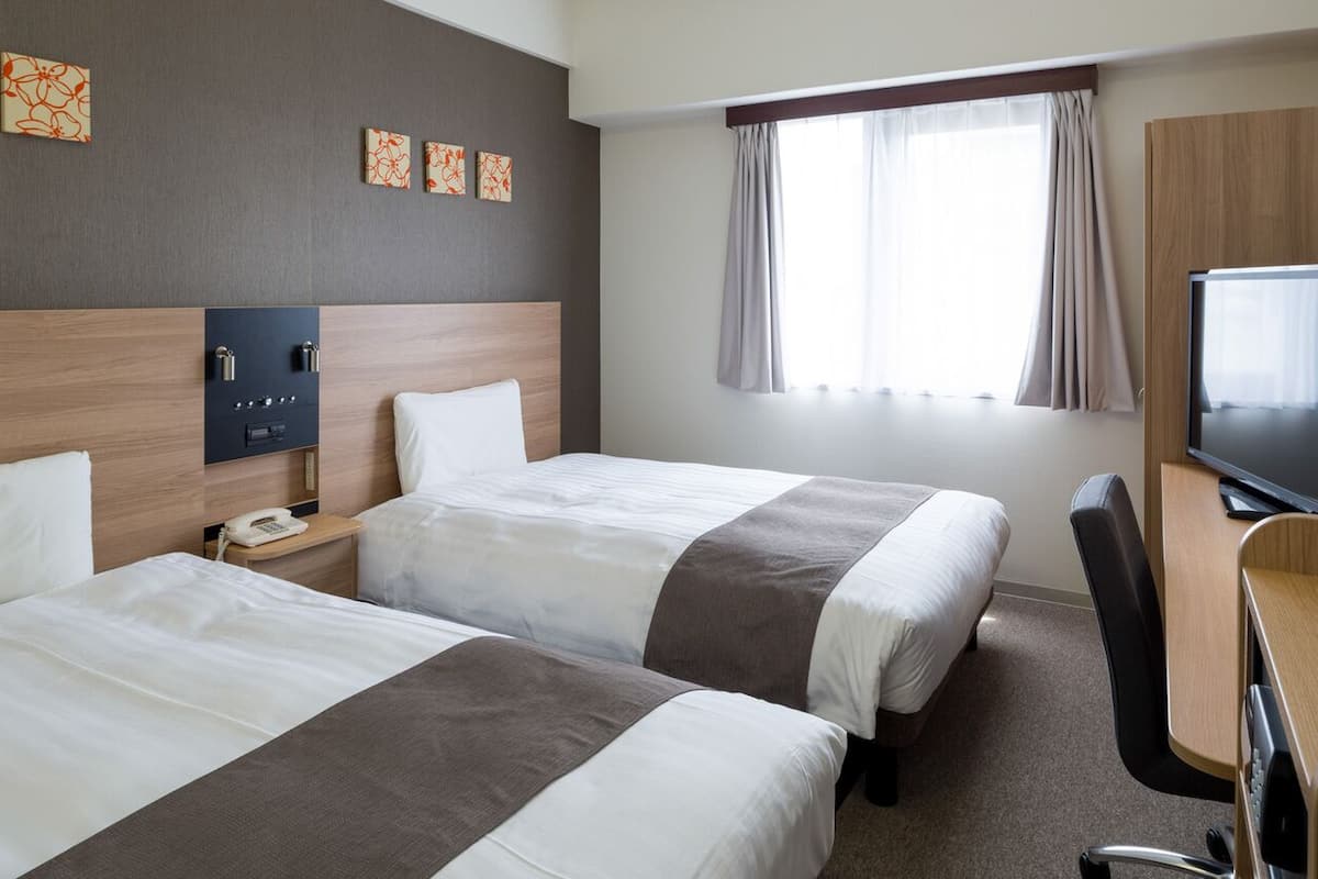A hotel room with two beds, a desk, a TV, and a phone.