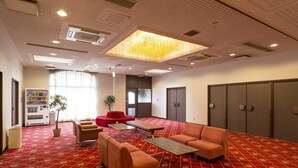 A spacious conference room with a red patterned carpet, a large window with curtains, a vending machine, and a potted plant. - Comfort Hotel Sakai (Sakai)
