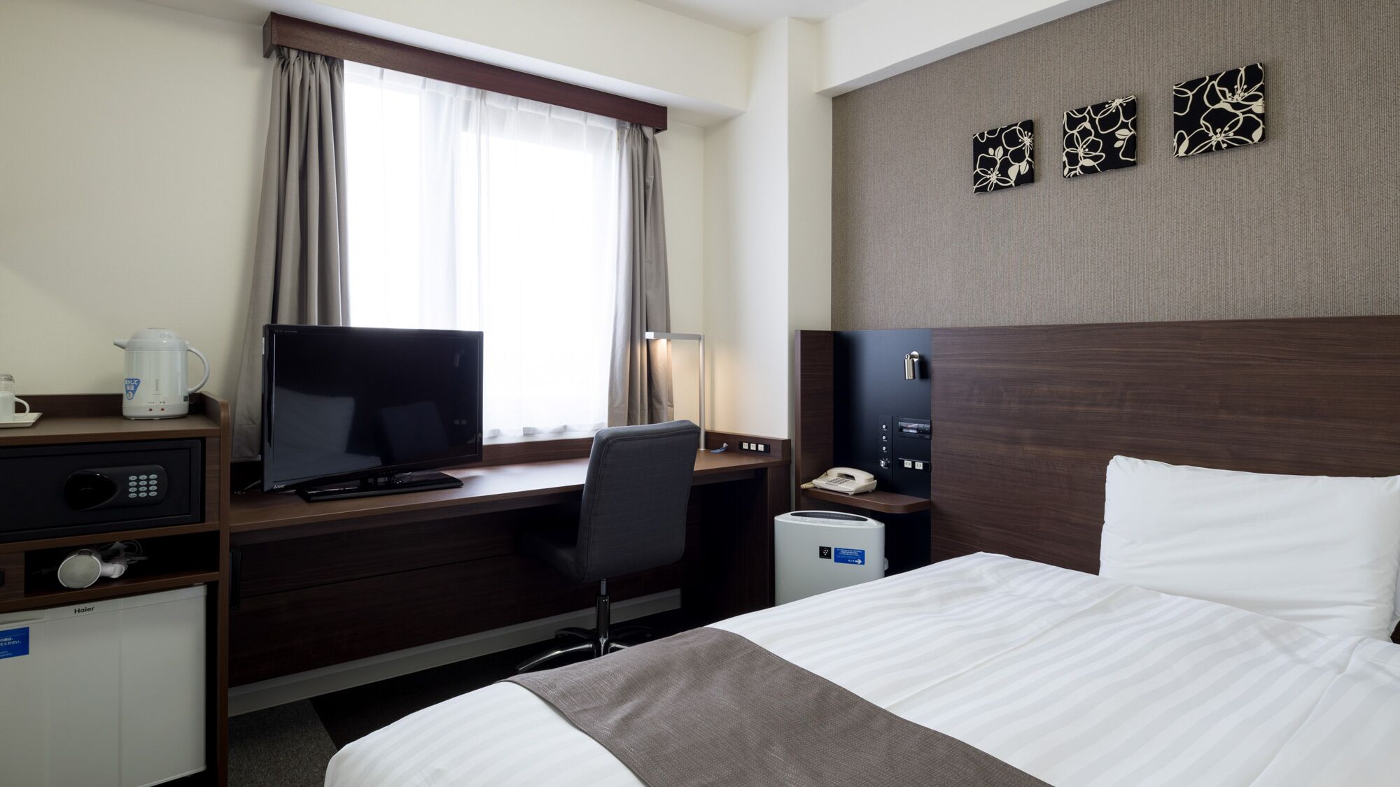 A hotel room with a bed, desk, television, and a window with curtains.