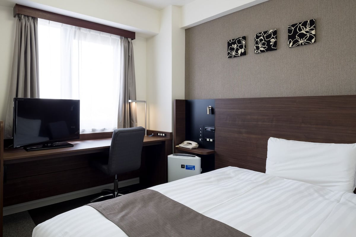 A hotel room with a bed, desk, television, and a window with curtains.