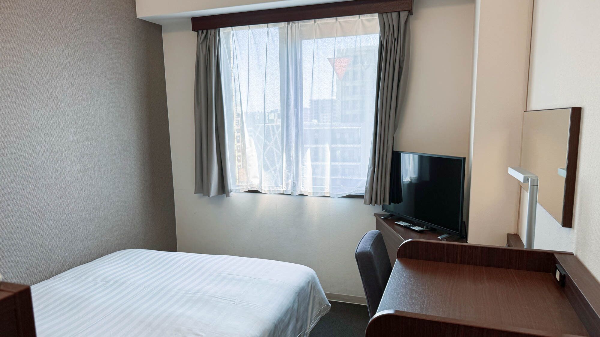 A hotel room with a bed, a desk, a television, and a window with curtains.