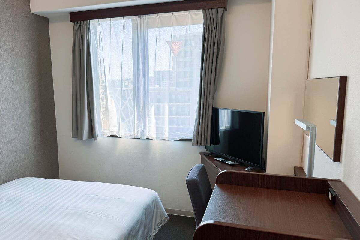A hotel room with a bed, a desk, a television, and a window with curtains.