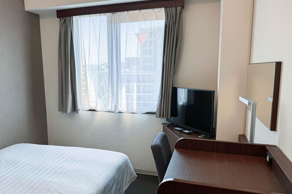 A hotel room with a bed, a desk, a television, and a window with curtains.
