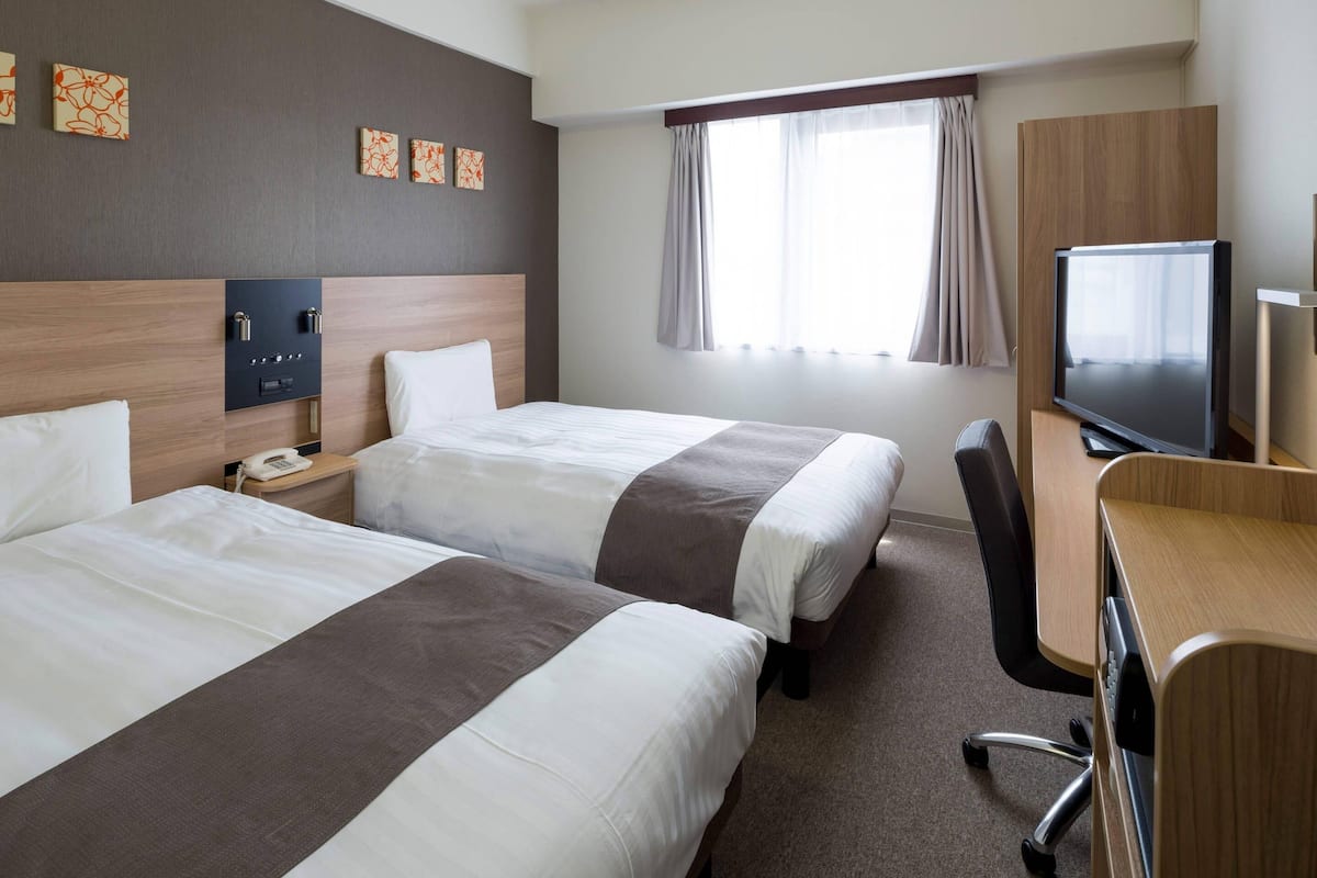 A hotel room with two beds, a desk with a TV, a phone, and a small table.