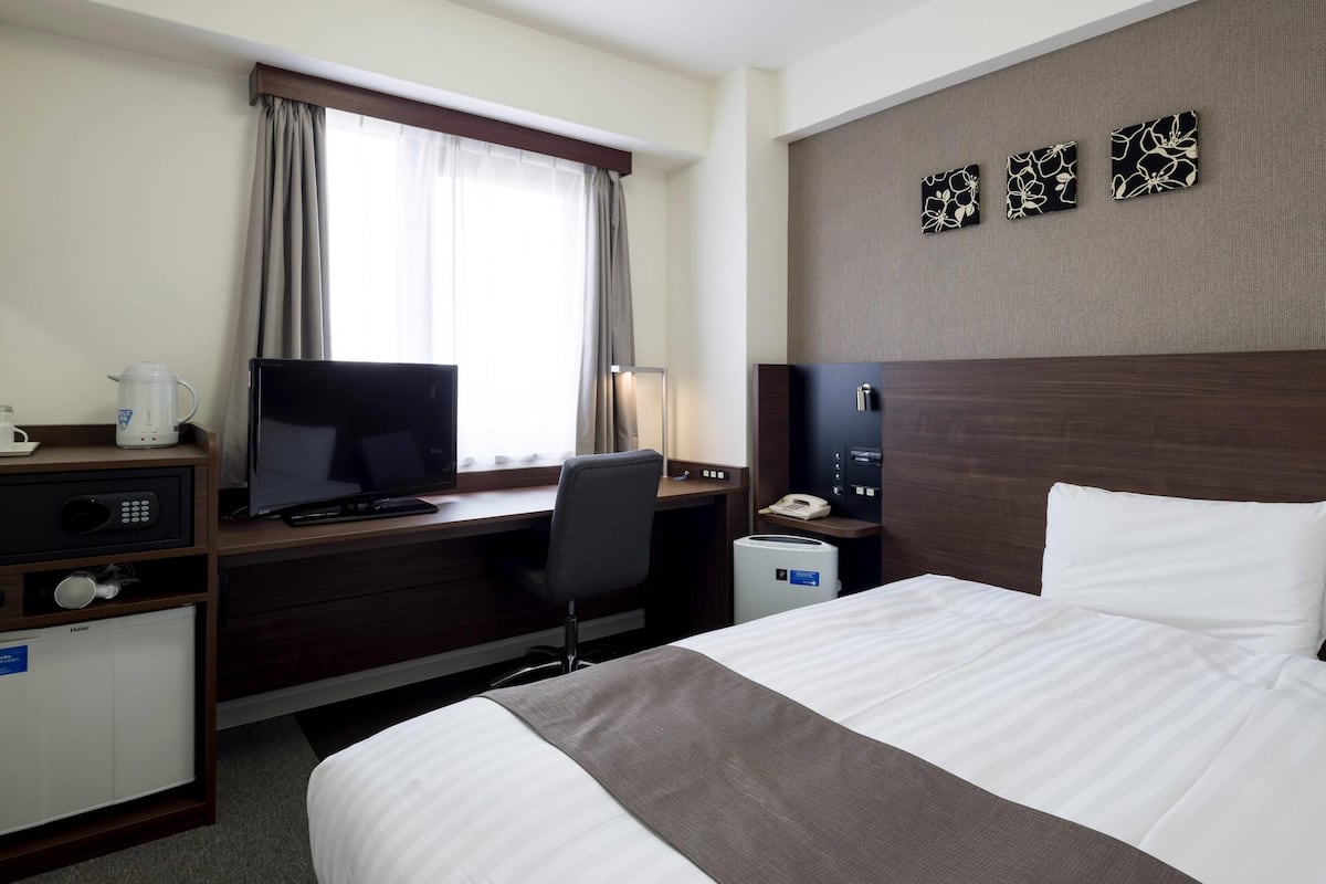 A hotel room with a bed, desk, television, and a small kitchenette.