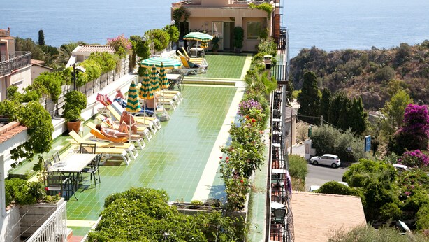 A rooftop pool with sun loungers and umbrellas, surrounded by greenery and overlooking a coastal area. - Hotel Ipanema (Taormina)