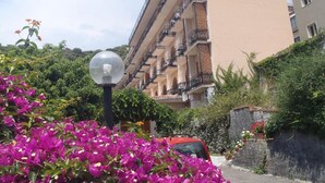 A multi-story building with balconies, surrounded by lush greenery and vibrant bougainvillea flowers. - Hotel Ipanema (Taormina)