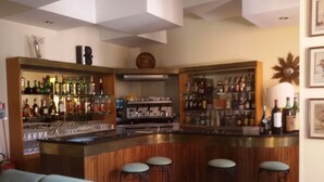 A bar area with stools, shelves of bottles, and a clock on the wall. - Hotel Ipanema (Taormina)