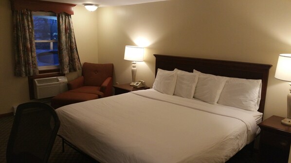 Une chambre d’hôtel avec un grand lit, une chaise, deux lampes de chevet, un téléphone et une fenêtre avec des rideaux.