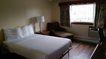 A hotel room with a bed, a chair, a nightstand, a lamp, and a window with curtains.