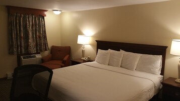 Habitación de hotel con una cama grande, dos lámparas de noche, una silla, un aire acondicionado y un teléfono en la mesita de noche.