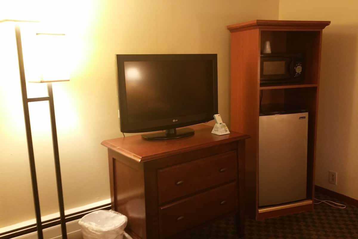 Una habitación de esquina con un armario de madera, un televisor de pantalla plana, un microondas y un cesto de basura.