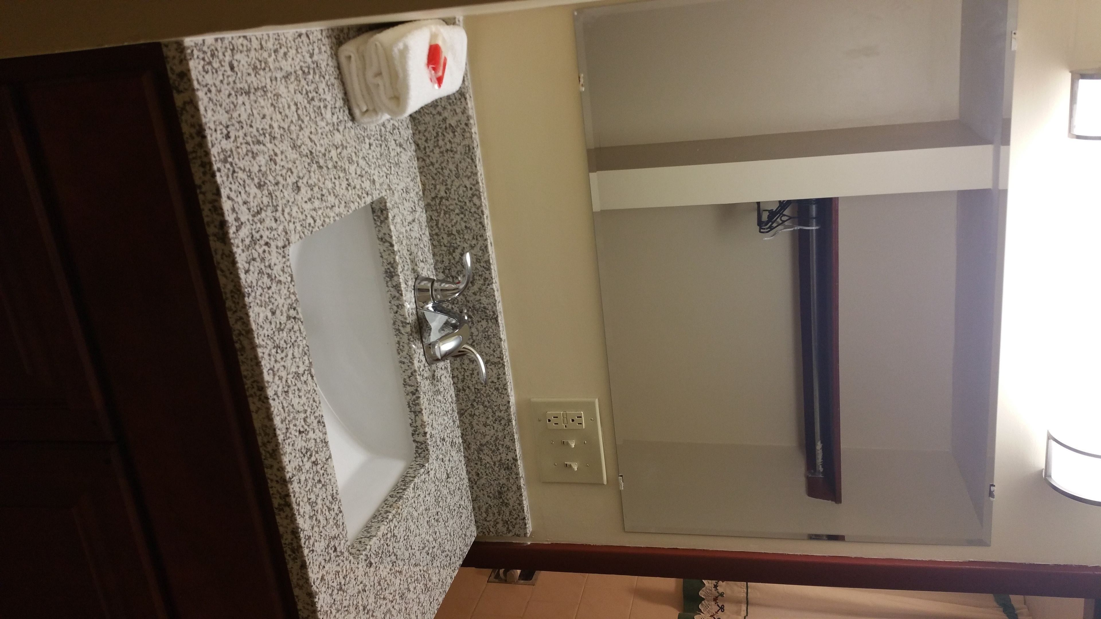 A bathroom with a granite countertop sink, a mirror, and a towel dispenser.