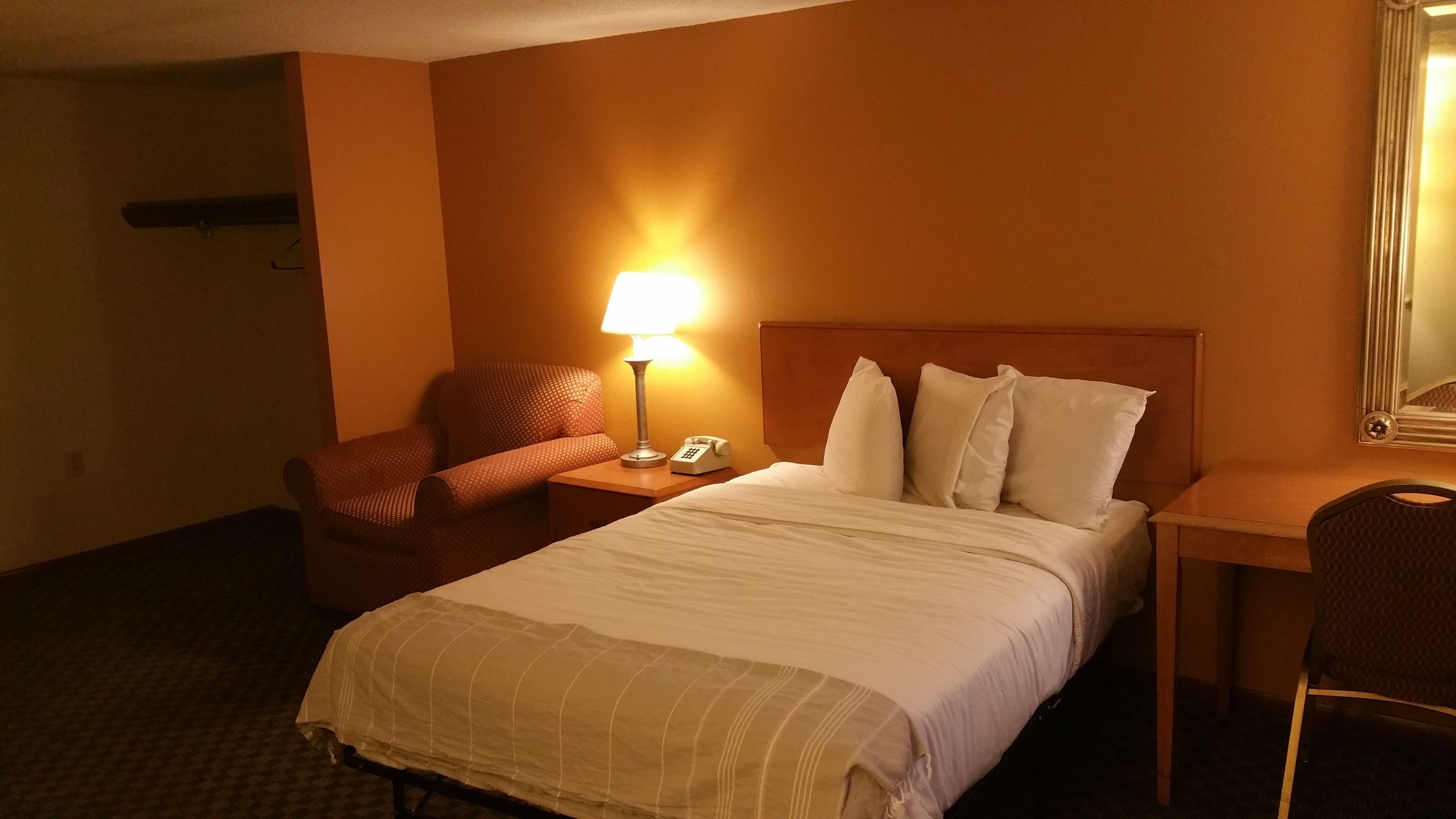 Quarto de hotel com cama, poltrona, escrivaninha, luminária e telefone.