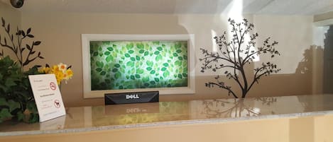 Una mesa de recepción con una computadora Dell, un letrero de bienvenida y un árbol decorativo.