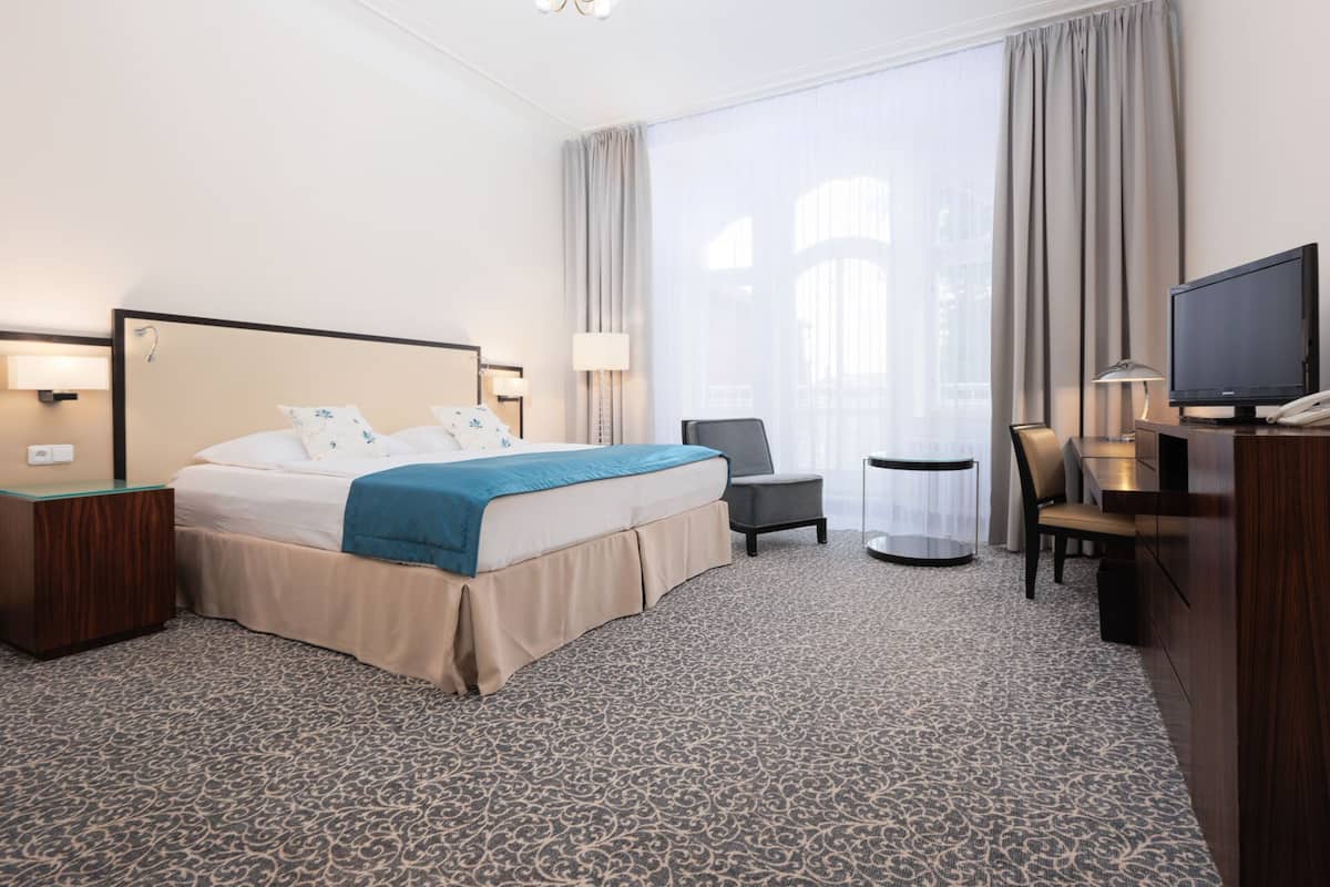 Ein Hotelzimmer mit einem großen Bett, einem Schreibtisch, einem Sessel und einem Fernseher.