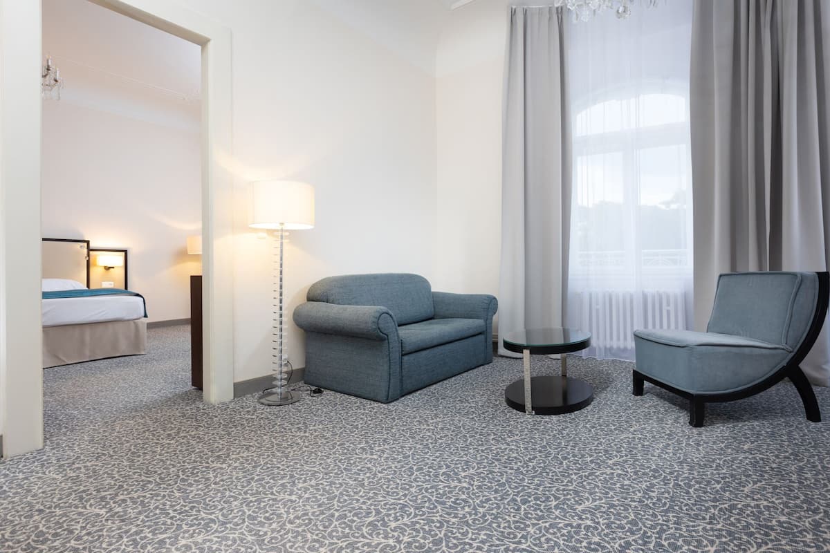 Ein Hotelzimmer mit einem Bett, einem blauen Sofa, einem Sessel, einer Stehlampe und einem Fenster mit Vorhängen.