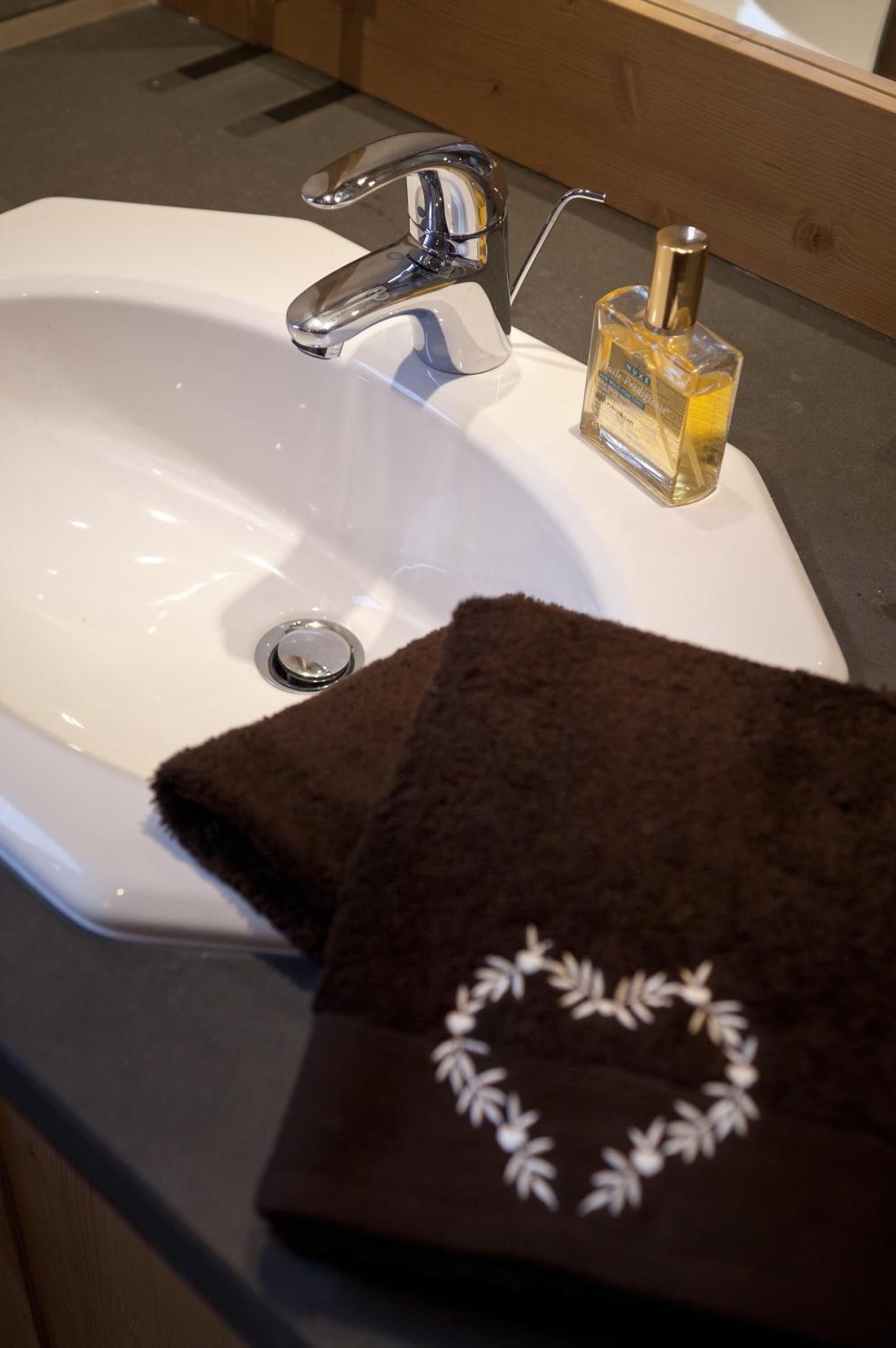 Ein Waschbecken mit chromfarbenem Wasserhahn, eine Handseifenflasche und zwei weiße Handtücher mit floralem Muster.