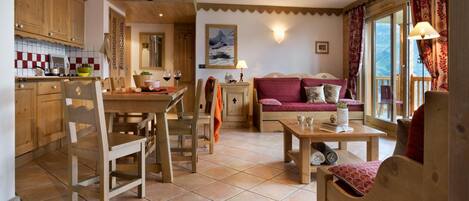 A cozy living room with a wooden sofa, a dining table, and a kitchen area with wooden cabinets and a tiled backsplash.